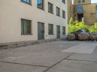 the street with parked cars next to tall buildings has large boulders all around it,