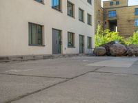 the street with parked cars next to tall buildings has large boulders all around it,