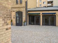 a brick walkway is next to an open building with many doors and windows on it