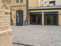 a brick walkway is next to an open building with many doors and windows on it