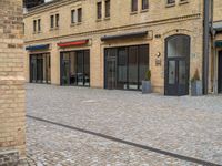 a brick walkway is next to an open building with many doors and windows on it