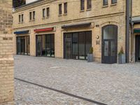 a brick walkway is next to an open building with many doors and windows on it