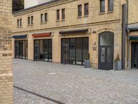 a brick walkway is next to an open building with many doors and windows on it