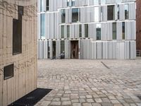 a person walking through an open courtyard of a building with glass doors and brick walkway