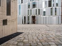 a person walking through an open courtyard of a building with glass doors and brick walkway