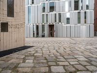 a person walking through an open courtyard of a building with glass doors and brick walkway