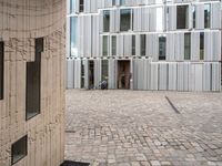 a person walking through an open courtyard of a building with glass doors and brick walkway