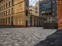 a sidewalk with chairs next to the brick building on the side, some have stairs and some buildings in the background