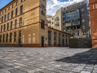 a sidewalk with chairs next to the brick building on the side, some have stairs and some buildings in the background