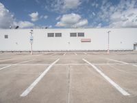 a large white building sitting next to a parking lot under blue skies and clouds on a clear day