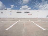 a large white building sitting next to a parking lot under blue skies and clouds on a clear day