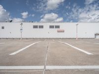 a large white building sitting next to a parking lot under blue skies and clouds on a clear day