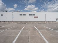 a large white building sitting next to a parking lot under blue skies and clouds on a clear day