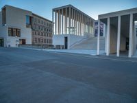 empty street lined with cement buildings next to a tall building with a staircase up to it