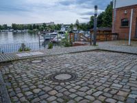 a paved area with two small water outlets on the brick pavement and several small boats in the water