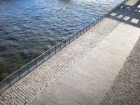 two people walk along a brick walkway with railings as it passes over the water