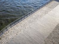 two people walk along a brick walkway with railings as it passes over the water