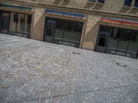 the sidewalk is paved with stones and has a bench in front of it, with no people inside