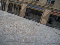 the sidewalk is paved with stones and has a bench in front of it, with no people inside