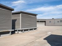 an empty parking lot near some large storage units and a building with corrugated siding and metal beams