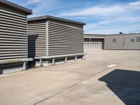 an empty parking lot near some large storage units and a building with corrugated siding and metal beams