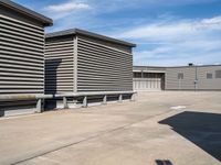 an empty parking lot near some large storage units and a building with corrugated siding and metal beams