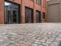 the sidewalk is paved with cobblestones that have black steel doors and windows,