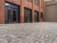 the sidewalk is paved with cobblestones that have black steel doors and windows,