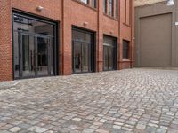 the sidewalk is paved with cobblestones that have black steel doors and windows,