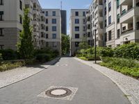 a cobblestone street with an outdoor seating area and parking spaces between two tall white apartment buildings