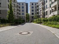 a cobblestone street with an outdoor seating area and parking spaces between two tall white apartment buildings