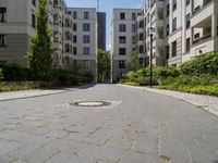 a cobblestone street with an outdoor seating area and parking spaces between two tall white apartment buildings