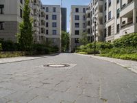 a cobblestone street with an outdoor seating area and parking spaces between two tall white apartment buildings