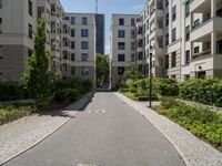 a cobblestone street with an outdoor seating area and parking spaces between two tall white apartment buildings