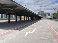 empty parking lot on concrete next to tall building with cranes in distance and buildings across the street