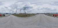 construction trucks on dirt road with large buildings in background and sky with white clouds above