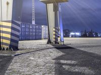 a red fire hydrant stands outside a container port in the rain at night, with a stop sign next to it