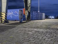 a red fire hydrant stands outside a container port in the rain at night, with a stop sign next to it