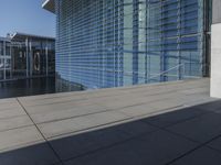 a large blue glass building next to water and buildings with blue windows and grey concrete flooring