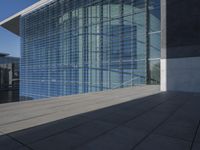 a large blue glass building next to water and buildings with blue windows and grey concrete flooring