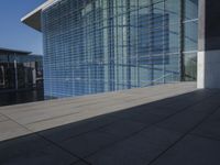 a large blue glass building next to water and buildings with blue windows and grey concrete flooring