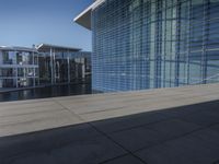 a large blue glass building next to water and buildings with blue windows and grey concrete flooring
