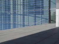 a large blue glass building next to water and buildings with blue windows and grey concrete flooring