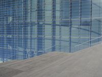 a large blue glass building next to water and buildings with blue windows and grey concrete flooring
