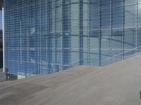 a large blue glass building next to water and buildings with blue windows and grey concrete flooring