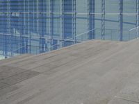 a large blue glass building next to water and buildings with blue windows and grey concrete flooring