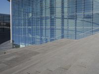 a large blue glass building next to water and buildings with blue windows and grey concrete flooring