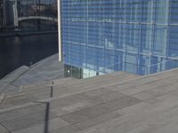 a large blue glass building next to water and buildings with blue windows and grey concrete flooring