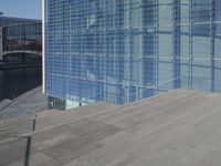 a large blue glass building next to water and buildings with blue windows and grey concrete flooring