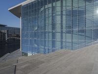 a large blue glass building next to water and buildings with blue windows and grey concrete flooring